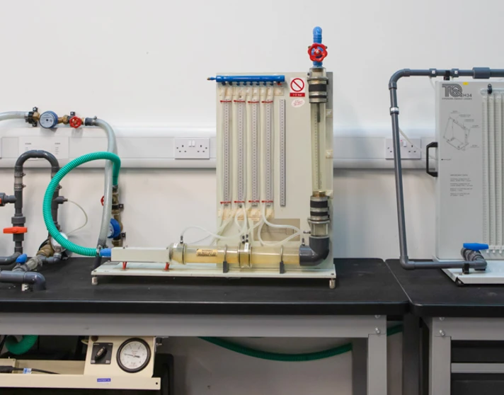 A set of fluid mechanics training rigs with interconnected pipes, valves, and flow meters, used for hands-on learning in a building services workshop. A set of fluid mechanics training rigs with interconnected pipes, valves, and flow meters, used for hands-on learning in a building services workshop.
